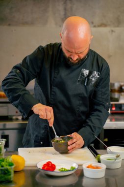 Profesyonel bir mutfakta siyah ceketli bir şef avokadoyu somonlu tost için hazırlar.