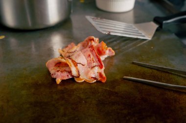 Profesyonel bir mutfakta, desenli bir masada kızarmış pastırma dilimleri var.