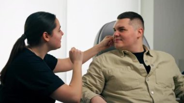 Bir kozmetoloji kliniğinde bir kız kozmetikçi bir erkekle ilk muayeneyi yapar.