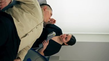 Kozmetik kliniğinde bir kız kozmetik uzmanı genç bir adamın yüzü için fotoğraf terapisi yapıyor.