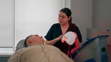 Bir kozmetoloji kliniğinde bir kız kozmetik uzmanı bir adama nasıl fotoğraf maskesi takılacağını söyler.