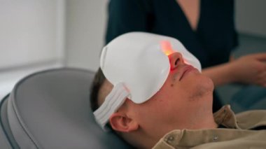 Bir kozmetoloji kliniğine yakın bir yerde bir kız kozmetik uzmanı bir adama nasıl fotoğraf maskesi takacağını söyler.