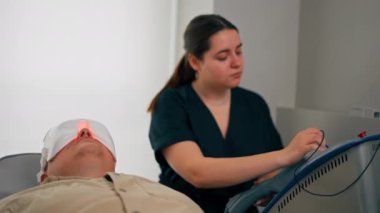 Bir kozmetoloji kliniğine yakın bir yerde bir kız kozmetik uzmanı bir adama nasıl fotoğraf maskesi takacağını söyler.
