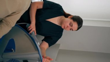 Bir kozmetoloji kliniğinde dikey video çekilirken bir kız kozmetik uzmanı bir adama nasıl fotoğraf maskesi takacağını söyler.