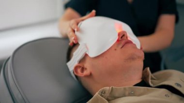 Bir kozmetoloji kliniğine yakın bir yerde bir kız kozmetik uzmanı bir adama fotoğraf maskesinin nasıl çıkarılacağını söyler.
