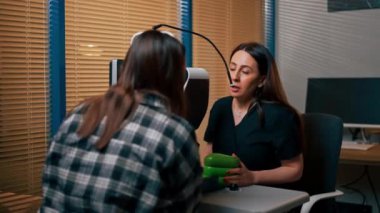 Bir göz hekiminde genç bir doktor büyüteçle genç bir kıza teşhis koyuyor.