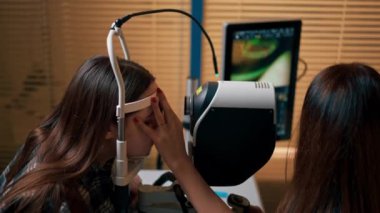 Bir göz hekimliği kliniğinde genç bir doktor büyüteçle genç bir kıza teşhis koyuyor.