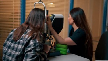 Bir göz hekiminde genç bir doktor büyüteçle genç bir kıza teşhis koyuyor.