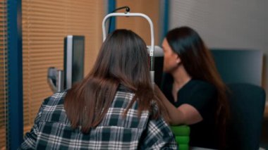 Bir göz hekiminde genç bir doktor büyüteçle genç bir kıza teşhis koyuyor.