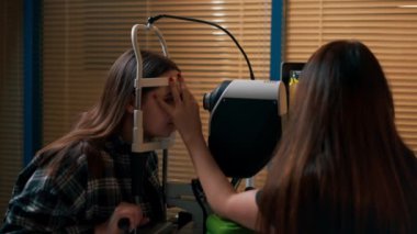 Bir göz hekiminde genç bir doktor büyüteçle genç bir kıza teşhis koyuyor.