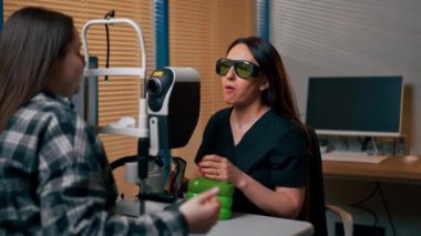 Bir göz hekiminde genç bir doktor büyüteçle genç bir kıza teşhis koyuyor.