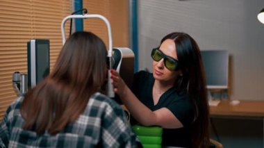 Bir göz hekiminde genç bir doktor büyüteçle genç bir kıza teşhis koyuyor.