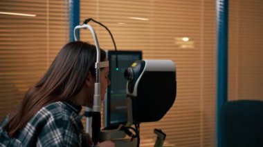 Bir göz hekiminde genç bir doktor büyüteçle genç bir kıza teşhis koyuyor.