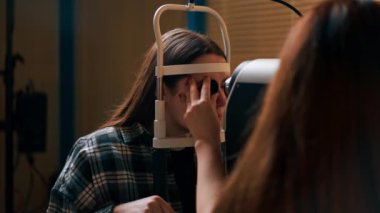 Bir göz hekiminde genç bir doktor büyüteçle genç bir kıza teşhis koyuyor.