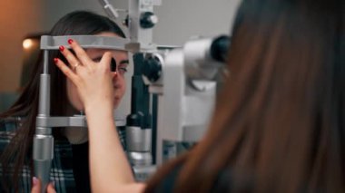 Bir göz hekimliği kliniğinde genç bir doktor büyüteçle genç bir kıza teşhis koyuyor.