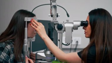 Bir göz hekiminde genç bir doktor büyüteçle genç bir kıza teşhis koyuyor.