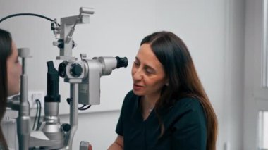 Bir göz hekiminde genç bir doktor büyüteçle genç bir kıza teşhis koyuyor.