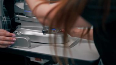 Bir göz hekimliği kliniğinde genç bir doktor büyüteçle genç bir kıza teşhis koyuyor.