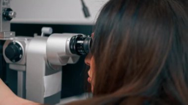 Bir göz hekimliği kliniğinde genç bir doktor büyüteçle genç bir kıza teşhis koyuyor.