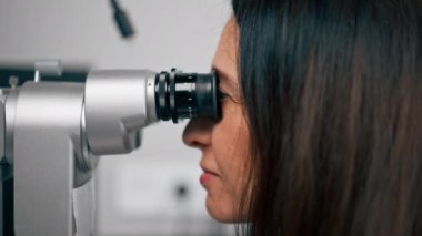 Bir göz hekimliği kliniğinde genç bir doktor büyüteçle genç bir kıza teşhis koyuyor.
