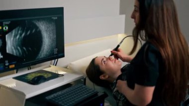Bir göz hekiminde genç bir doktor genç bir kızın gözünün ultrasonunu çeker.