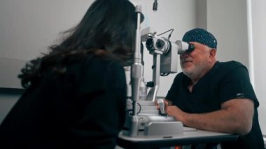 Optalmoloji kliniğinde yaşlı doktor büyüteçle genç bir kıza teşhis koyuyor.