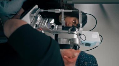 Optalmoloji kliniğindeki dikey video. Yaşlı doktor, büyüteç takan bir kıza teşhis koydu.