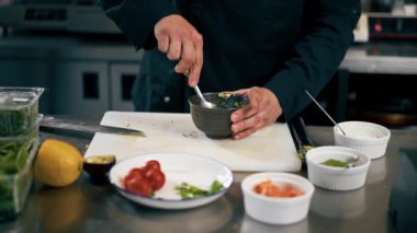 Profesyonel bir mutfakta siyah ceketli bir şef avokadoyu somonlu tost için hazırlar.