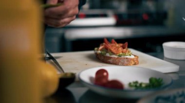 Profesyonel bir mutfak şefi siyah ceketli somon balığını cımbızla tost yapar.