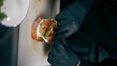 Profesyonel bir mutfak aşçısının siyah ceketli videosu somon balığını yapraklı tostla süslüyor.