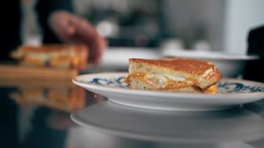 Profesyonel bir mutfakta yakın plan çekimde şef peynirli tostu tabağa koyar.