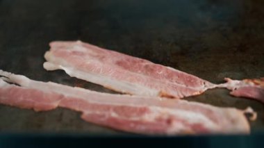 Profesyonel bir mutfakta yakın plan bir aşçı fırında domuz pastırması kızartıyor.