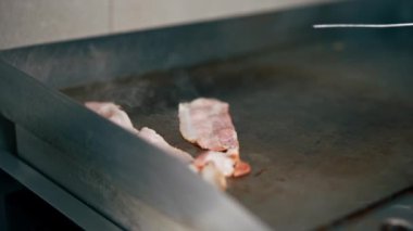 Profesyonel mutfakta yakın plan çekimde şef cımbız kullanarak fırında domuz pastırması pişiriyor.