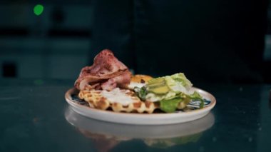 Profesyonel bir mutfakta siyah ceketli bir aşçı Belçika usulü sebzeli waffle yapıyor.