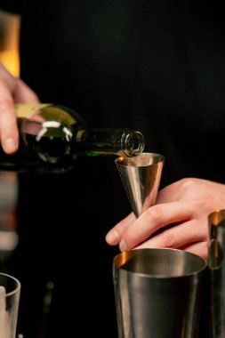 Yakın plan erkek barmen elleri şişeyi tutuyor ve içeceği ustalıkla jigger 'a dolduruyor.