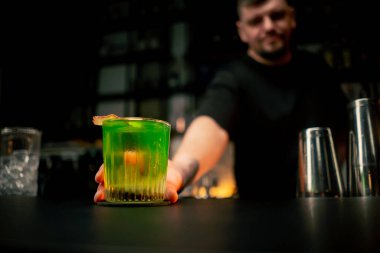 Barmen elinde bir bardak dolusu taze yeşil kokteyl tutuyor. Ekşi ve tatlı.