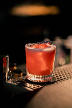 Çelik tezgahta duran çiçekli lezzetli kırmızı kokteyl ve bulanık arka planda duran tahta tezgah.