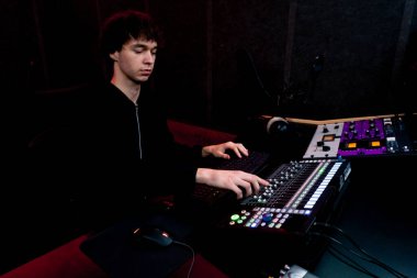 Kayıt odasının karanlığında stüdyoda neon ışıkla birlikte ses mühendisi konsolda çalışır sesi ayarlar ve sesi karıştırır.