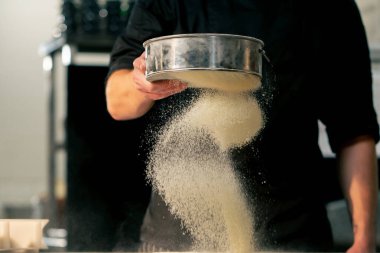 Bir pizzacının profesyonel mutfağında yakın plan çekimde şef masayı un ile sarıyor.