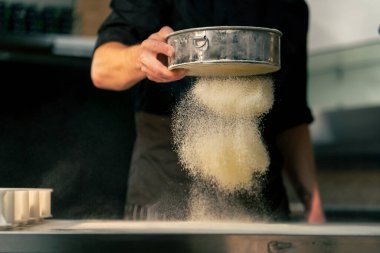 Bir pizzacının profesyonel mutfağında yakın plan çekimde şef masayı un ile sarıyor.