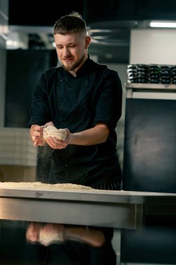 Profesyonel bir mutfakta, pizzacıda siyah üniformalı genç bir şef pizza hamuru hazırlıyor.