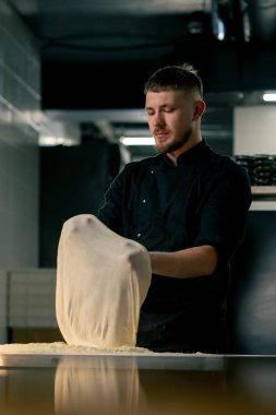 Profesyonel bir mutfakta, pizzacıda siyah üniformalı genç bir şef pizza hamuru hazırlıyor.