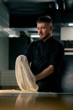 Profesyonel bir mutfakta, pizzacıda siyah üniformalı genç bir şef pizza hamuru hazırlıyor.