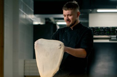 Profesyonel bir mutfakta, pizzacıda siyah üniformalı genç bir şef pizza hamuru hazırlıyor.