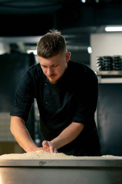 Profesyonel bir mutfakta, pizzacıda siyah üniformalı genç bir şef pizza hamuru hazırlıyor.