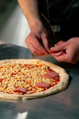 Bir pizzacının profesyonel mutfağında siyah üniformalı genç bir şef pizzanın içine malzeme koyar.