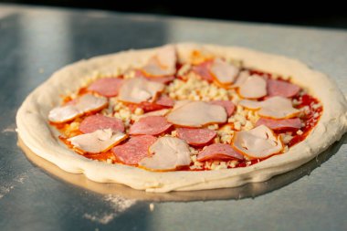 Profesyonel bir mutfağa yakın plan. Masada fırına atılmaya hazır taze pişmiş pizza var.