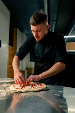 Profesyonel bir mutfakta bir pizzacıda siyahlı genç bir şef spatulayla fırın için çiğ pizza alır.