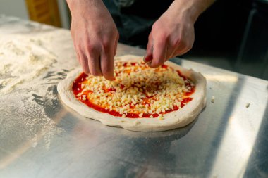 Bir pizzacının profesyonel mutfağında siyah üniformalı genç bir şef pizzanın içine malzeme koyar.