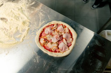 Profesyonel bir mutfakta yakın plan çekimde masada fırına atılmaya hazır taze pişmiş pizza var.